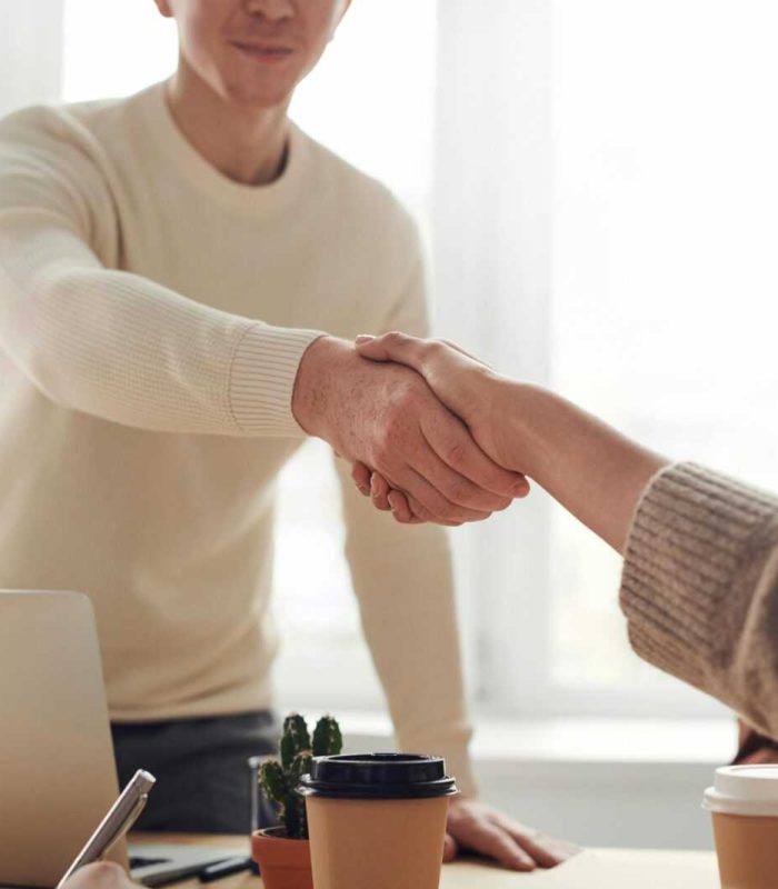 Close-up of professionals shaking hands over coffee in a modern office.