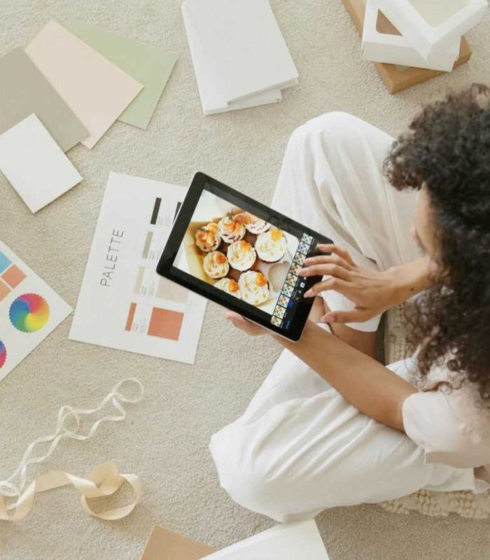 Woman using tablet surrounded by design tools and gift box, showcasing creativity and online work.