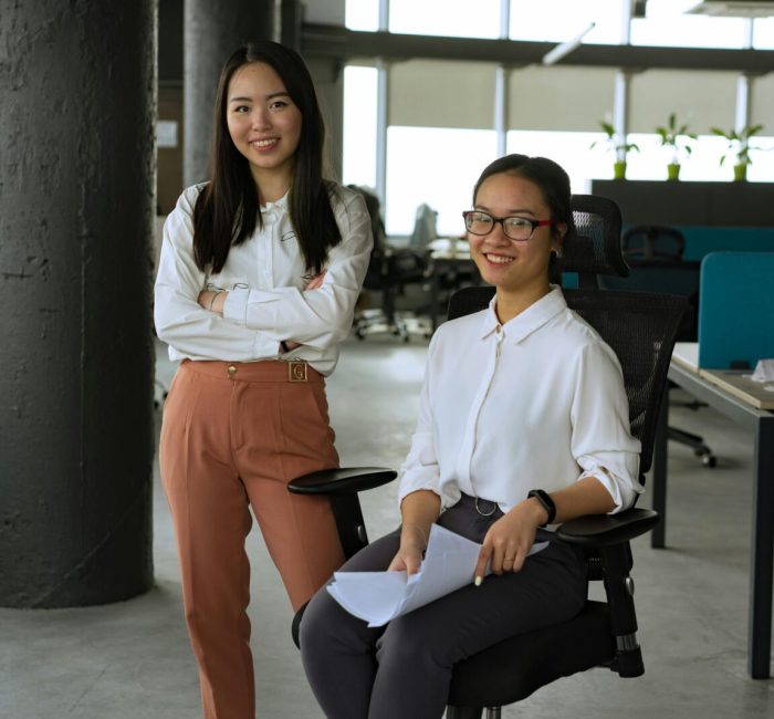 Two women in a contemporary office, smiling and interacting, promoting teamwork and collaboration.