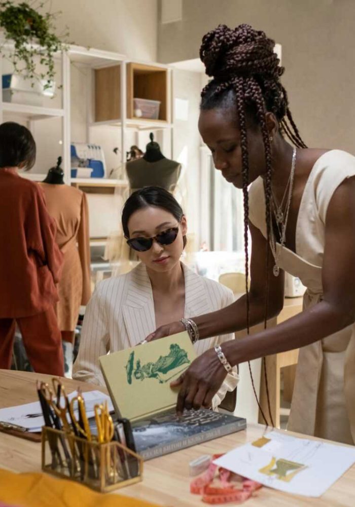 Two fashion designers collaborate in a sunlit studio, analyzing a sketch and discussing ideas.